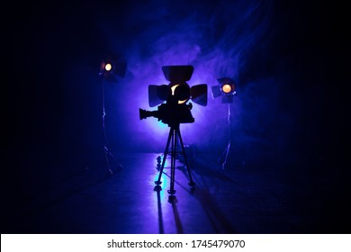 Movie Concept. Miniature Movie Set On Dark Toned Background With Fog And Empty Space. Silhouette Of Vintage Camera On Tripod. Selective Focus