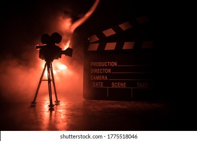 Movie Concept. Miniature Movie Set On Dark Toned Background With Fog And Empty Space. Silhouette Of Vintage Camera On Tripod And Clapboard. Selective Focus