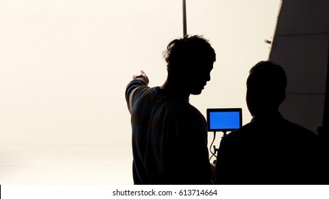 Movie Director And Photographer Are Talking Or Consulting To Making Studio Set Before Shooting Video And Silhouette Background Lighting.