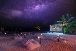 Movie Night On Starry Tropical Island Beach. Amazingly Calm And Relaxed Scenic View Of Outdoor Cinema With The Milky Way And Palm Trees With Soft Candle Light. Summer Family Holiday, Luxury Lifestyle