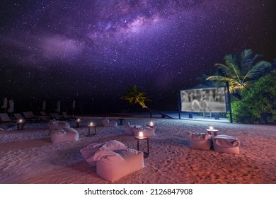 Movie night on starry tropical island beach. Amazingly calm and relaxed scenic view of outdoor cinema with the Milky Way and palm trees with soft candle light. Summer family holiday, luxury lifestyle