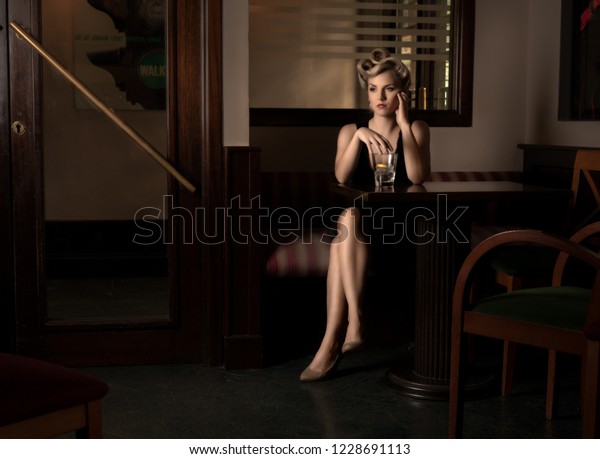 Movie scene with a femme fatal waiting in a\
restaurant with a glass of\
alcohol.