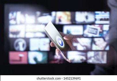 Movie stream smart app in mobile phone with many thumbnails of online video content. Man watching series with smartphone. Futuristic hologram interface around screen. Subscribe to entertainment. - Shutterstock ID 1452139691
