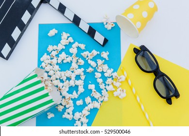 Movie Tickets, Clapperboard, Pop Corn And 3d Glasses In A White, Blue And Yellow Background.Flatlay