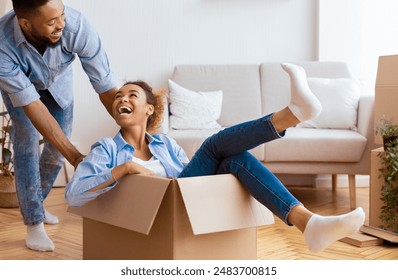 Moving Apartment. Excited Black Man Riding Girlfriend In Cardboard Box Having Fun In New Home. Selective Focus - Powered by Shutterstock