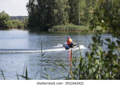 Moving Away Inflatable Motor Boat With Outboard Motor And  Man In Orange Lifejacket Fast Floating On The Water On Green Trees Background At Sunny Summer Day, Beautiful Russian River Landscape