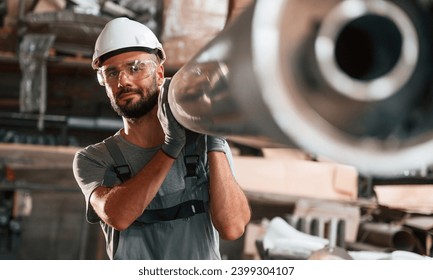 Moving big metal pipe. Young factory worker in grey uniform. - Powered by Shutterstock