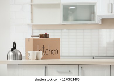 Moving box, dishware and adhesive tape dispenser on table indoors. Space for text - Shutterstock ID 1190821495