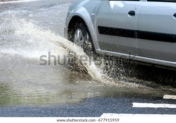Moving car sprays puddle when heavy rain drops\
on concrete.