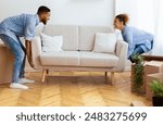 Moving Concept. Cheerful Afro Spouses Placing Couch Furnishing Empty Room In New House After Relocation