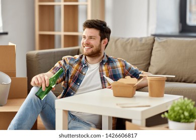 Moving, Consumption And People Concept - Smiling Man Eating Takeaway Food And Drinking Beer From Bottle At New Home