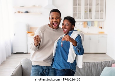 Moving Day. Happy African American couple holding and showing keys of their new apartment house, man shaking clenched fist. Excited homeowners enjoying and celebrating relocation