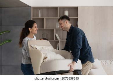 Moving day  happy buyers fashionable furniture  bank mortgage concept  Smiling loving millennial wife   husband carry new armchair into living room  making home design improvements feel satisfied