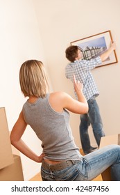 Moving House: Couple Hanging Picture On Wall In New Home