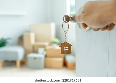Moving house, relocation. The key was inserted into the door of the new house, inside the room was a cardboard box containing personal belongings and furniture. move in the apartment or condominium - Shutterstock ID 2281919651