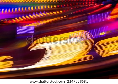 Moving lights of a Merry-go-round or carousel with colorful violiet, red, yellow, pink and orange illumination. Blurred lights traces and spots taken with Long Time Exposure on a fun fair in Germany. 
