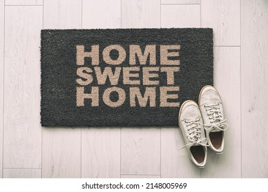 Moving In New Condo Apartment Home Sweet Home Text Doormat At House Entrance With Women's Sneakers Of Woman That Has Just Arrived. Home Background,