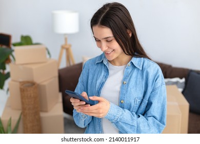 Moving To A New House, Rental Housing. Happy Young Caucasian Woman Using A Mobile Phone To Search And Order A Transportation Service And Movers To Move To A New Home