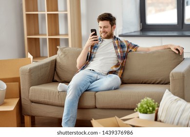 moving, people and real estate concept - happy man with smartphone and boxes sitting on sofa at new home - Shutterstock ID 1439376986