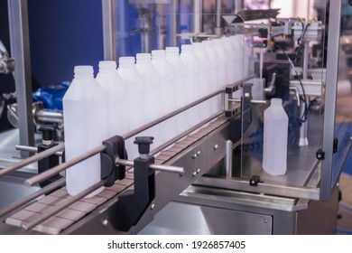 Moving polypropylene white bottles on conveyor belt of automatic liquid filling machine at plastic exhibition, trade show. Manufacturing, industry and automated technology equipment concept