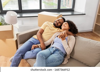 Moving, Repair And Real Estate Concept - Happy African American Couple With Cardboard Boxes Sitting On Sofa At New Home