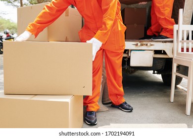 Moving Service Worker In Bright Orange Overall And Glover Putting Big Cardboard Boxes In Delivery Truck