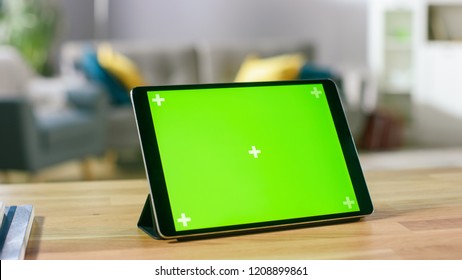 Moving Shot of the Green Mock-up Screen Digital Tablet Computer Standing on a Desk in Landscape Mode. In the Background Depth of Field Cozy Living Room.