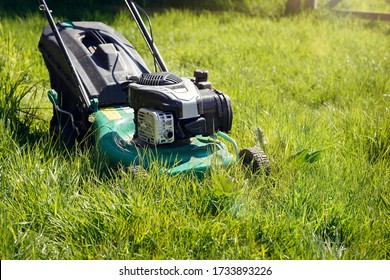 Mowing Or Cutting The Very Long Grass With A Green Lawn Mower In The Summer Sun