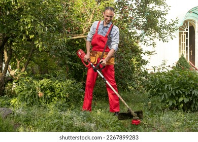 Mowing grass with electric lawn mower. Garden work concept. Man mows the grass with hand mower in the garden - Shutterstock ID 2267899283
