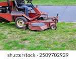 Mowing grass in park with lawn mower tractor at landscaping works is performed by municipal employee