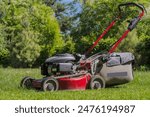 Mowing the grass with a petrol lawnmower. A petrol lawnmower standing at the edge of an area with mowed grass.