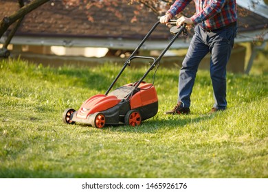 Mowing Trimmer - Worker Cutting Grass In Green Yard At Sunset. Man With Electric Lawnmower, Lawn Mowing. Gardener Trimming A Garden