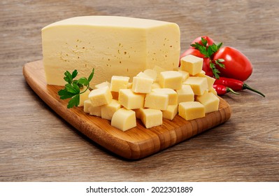 Mozzarella cheese in pieces and cut into cubes on wooden cutting board on wooden background.