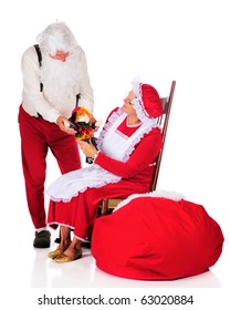 Mr. And Mrs. Santa Clause Admiring A Doll Before Putting It Into Santa's Sack.  Isolated On White.