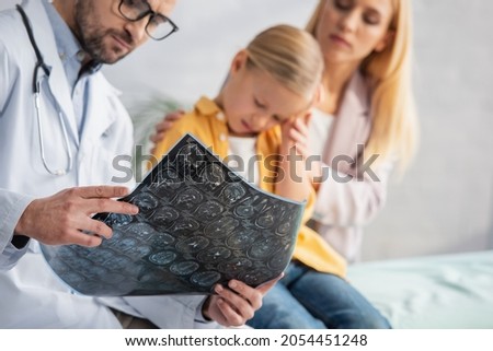 Mri scan in hands of blurred pediatrician near sad kid and woman in clinic
