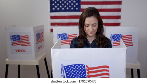 MS front view Caucasian American woman in plaid shirt in voting booth, casting vote at polling station. US flag on wall in background