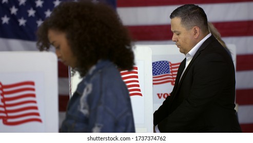 MS Hispanic Man At Polling Station, Votes In A Booth With Young Hispanic Woman In Foreground And Blonde Caucasian Woman Behind And US Flag In Background