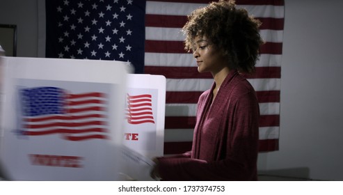 MS Young mixed-race woman ready to vote with blurred voting booth in foreground, being removed. Symbol of disenfranchisement with US flag backdrop - Shutterstock ID 1737374753
