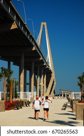 Mt Pleasant, SC, USA June 23 Two adults walk along a small pier at the foot of the Ravenel Bridge in Mt Pleasant, South Carolina.  The bridge connects Mt Pleasant with Charleston