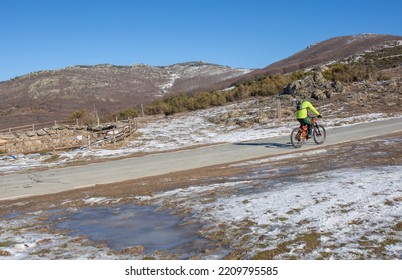 MTB Biker Climbing Mountain Pass. Roadside With Snow And Ice Ponds