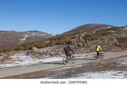 MTB Bikers Climbing Mountain Pass. Roadside With Snow And Ice Ponds