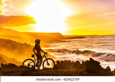 MTB cyclist mountain biking woman cycling looking at view on bike trail on coast at sunset. Person on bike by sea in sportswear with bicycle enjoying healthy active lifestyle in beautiful nature.