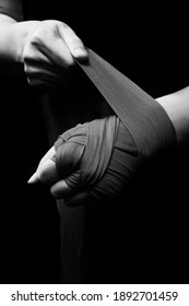 Muay Thai female boxer wearing strap on wrist closeup view. Fitness young woman preparing for boxing training on black background, monochrome