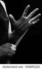 Muay Thai female boxer wearing strap on wrist closeup view. Fitness young woman preparing for boxing training on black background, monochrome