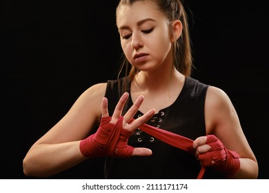 Muay Thai female boxer wearing strap on wrist closeup view. Fitness young woman preparing for boxing training on black background