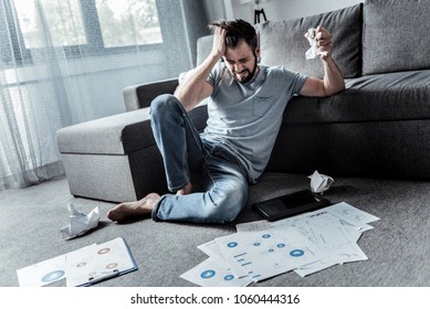 Its too much. Depressed angry young man sitting on the floor and being surrounded by papers while not coping with his work