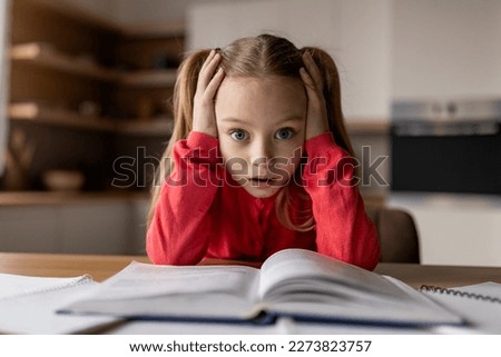 Too Much Homework. Closeup Shot Of Shocked Little Schoolgirl Touching Head While Sitting At Desk At Home, Panicked Preteen Female Child Looking At Camera, Having Problems With School Tasks