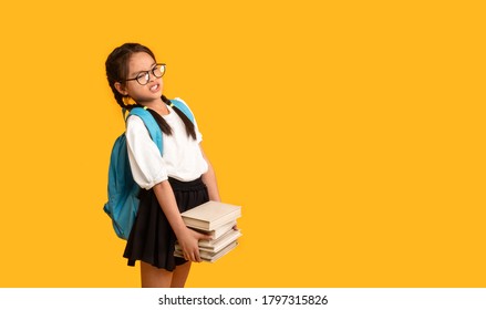 Too Much Homework. Discontented Asian School Girl Carrying Heavy Books Over Yellow Studio Background. Copy Space