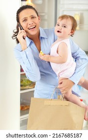 Too Much To Juggle Sometimes. An Overwhelmed Working Mom Speaking On The Phone While Holding Her Baby And A Bag Of Groceries.