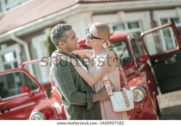 So much love. Beautiful\
married couple hugging each other standing in front of their opened\
retro-car.